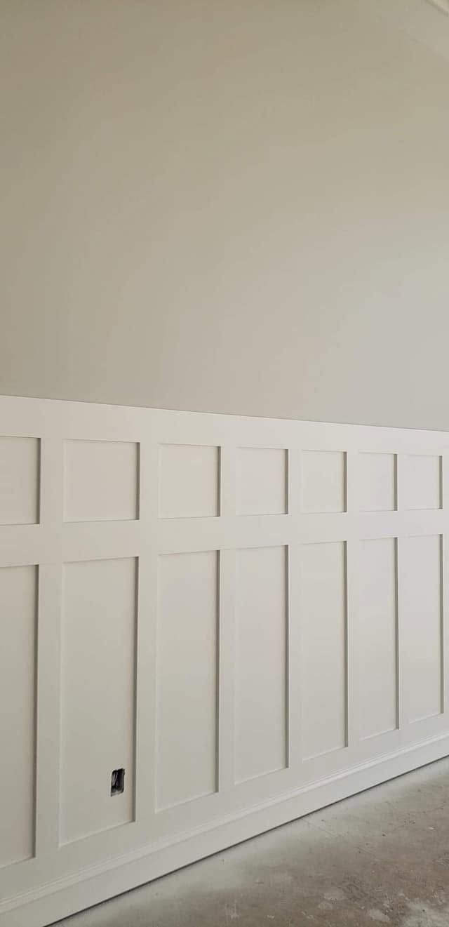 White paneled wainscoting along a beige wall in an unfinished interior room, with a concrete floor