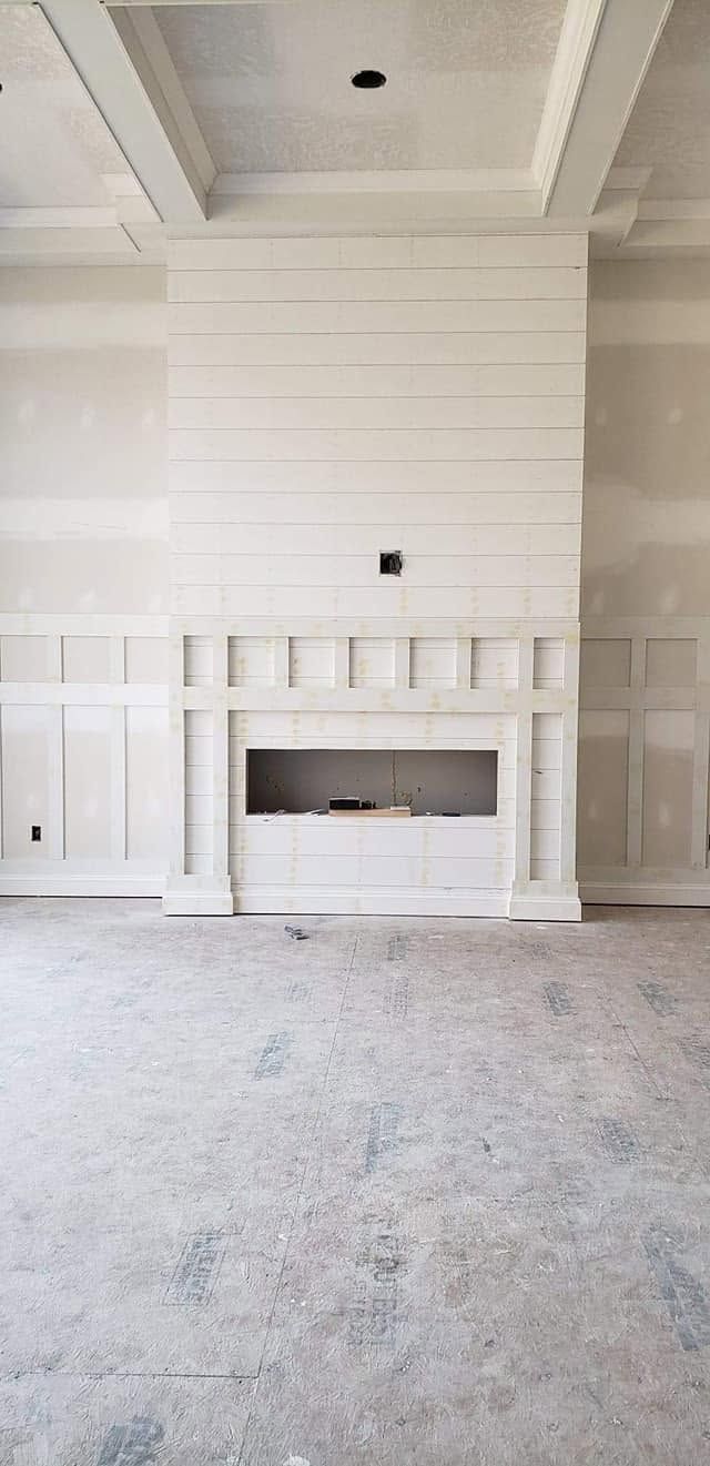 White paneled fireplace wall with a small rectangular firebox and carpeted floor in a room under construction