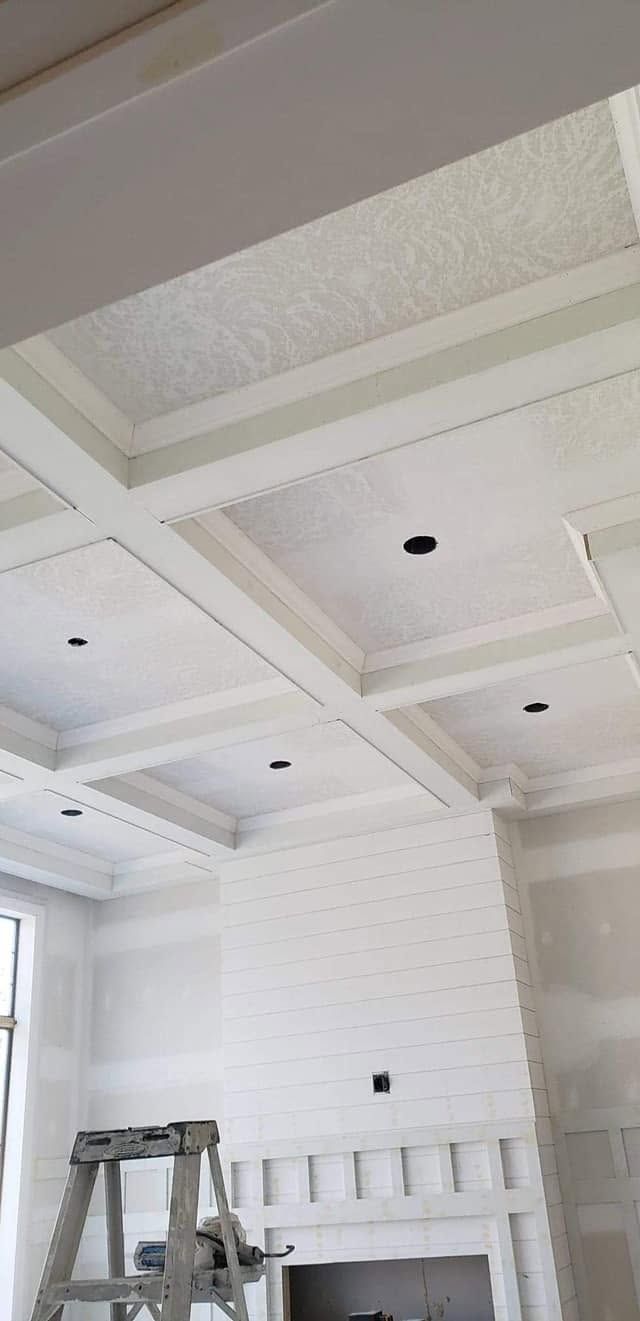 White room interior with coffered ceiling, recessed light cutouts, and a ladder near a window
