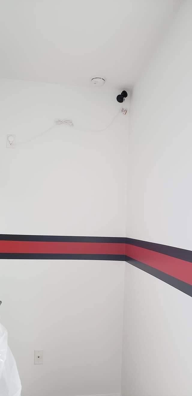 Empty white room with a red-and-black horizontal wall stripe and a ceiling corner camera.