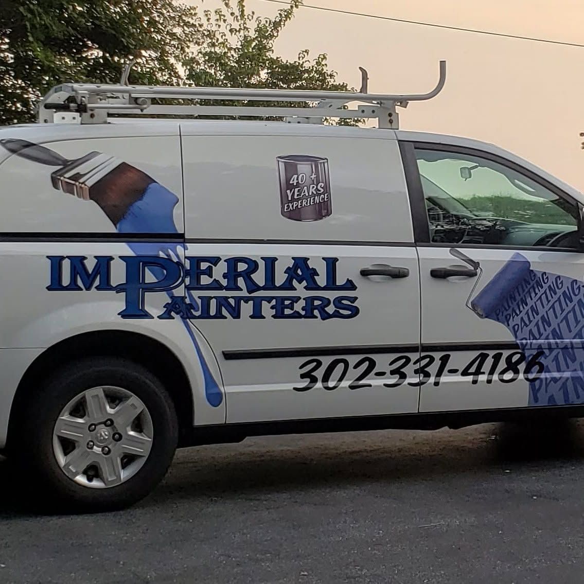 White Imperial Painters van with ladder rack and phone number parked on a street at dusk