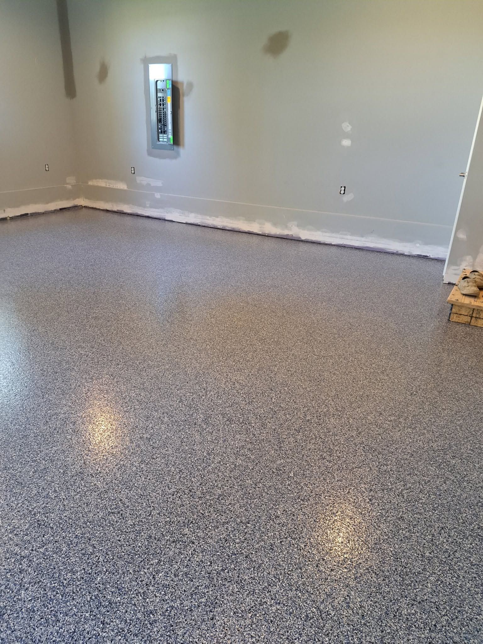 Empty room with gray speckled flooring, light walls, and a narrow window.