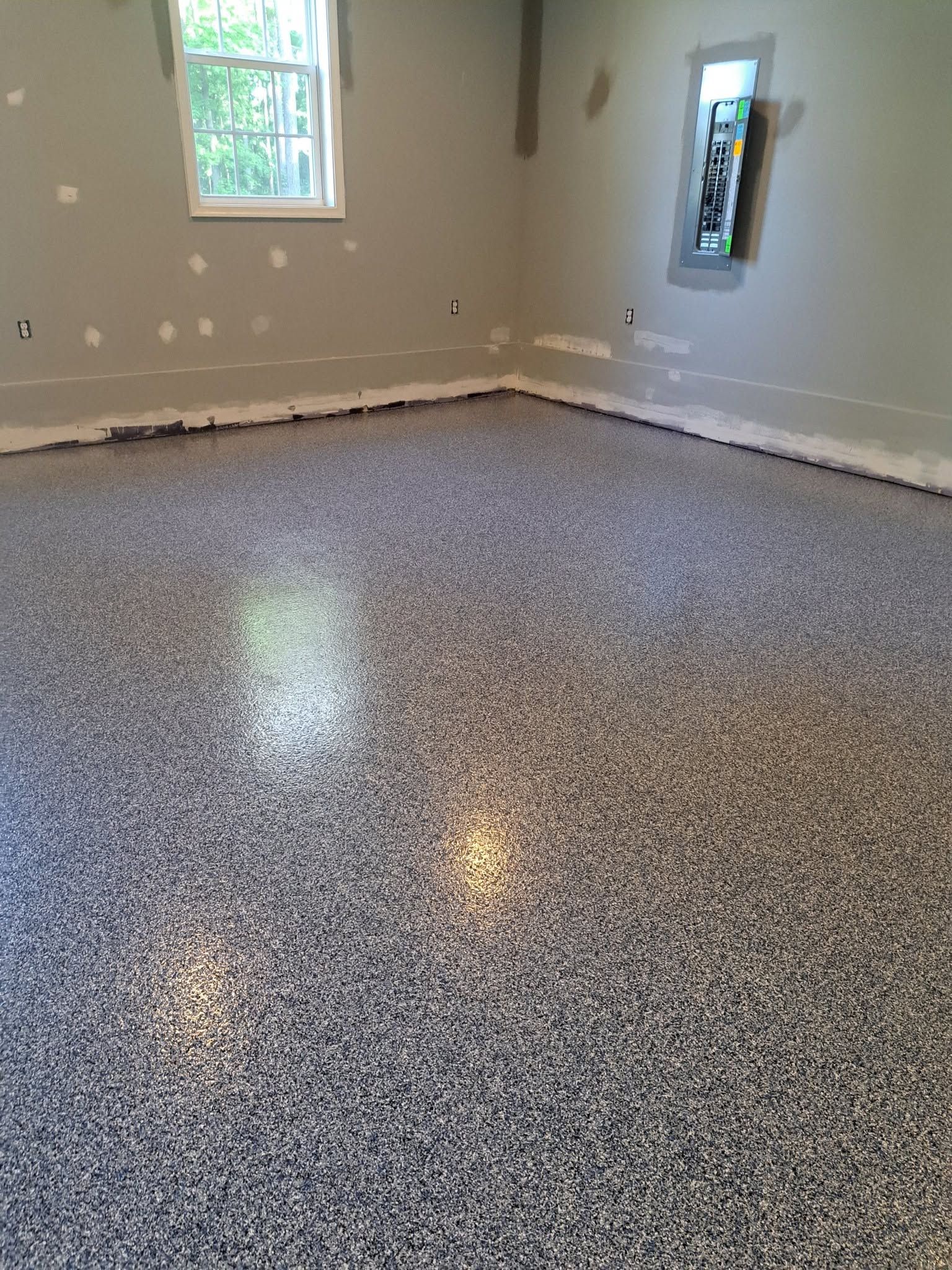 Empty room with speckled epoxy floor, beige walls, and two small windows.
