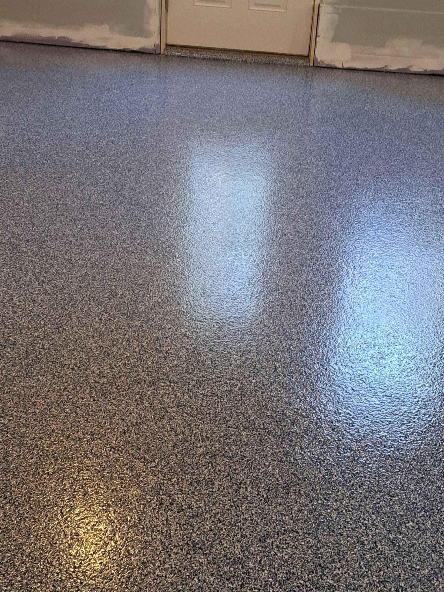 Speckled gray and black polished floor with reflections of light near a wall and cabinets