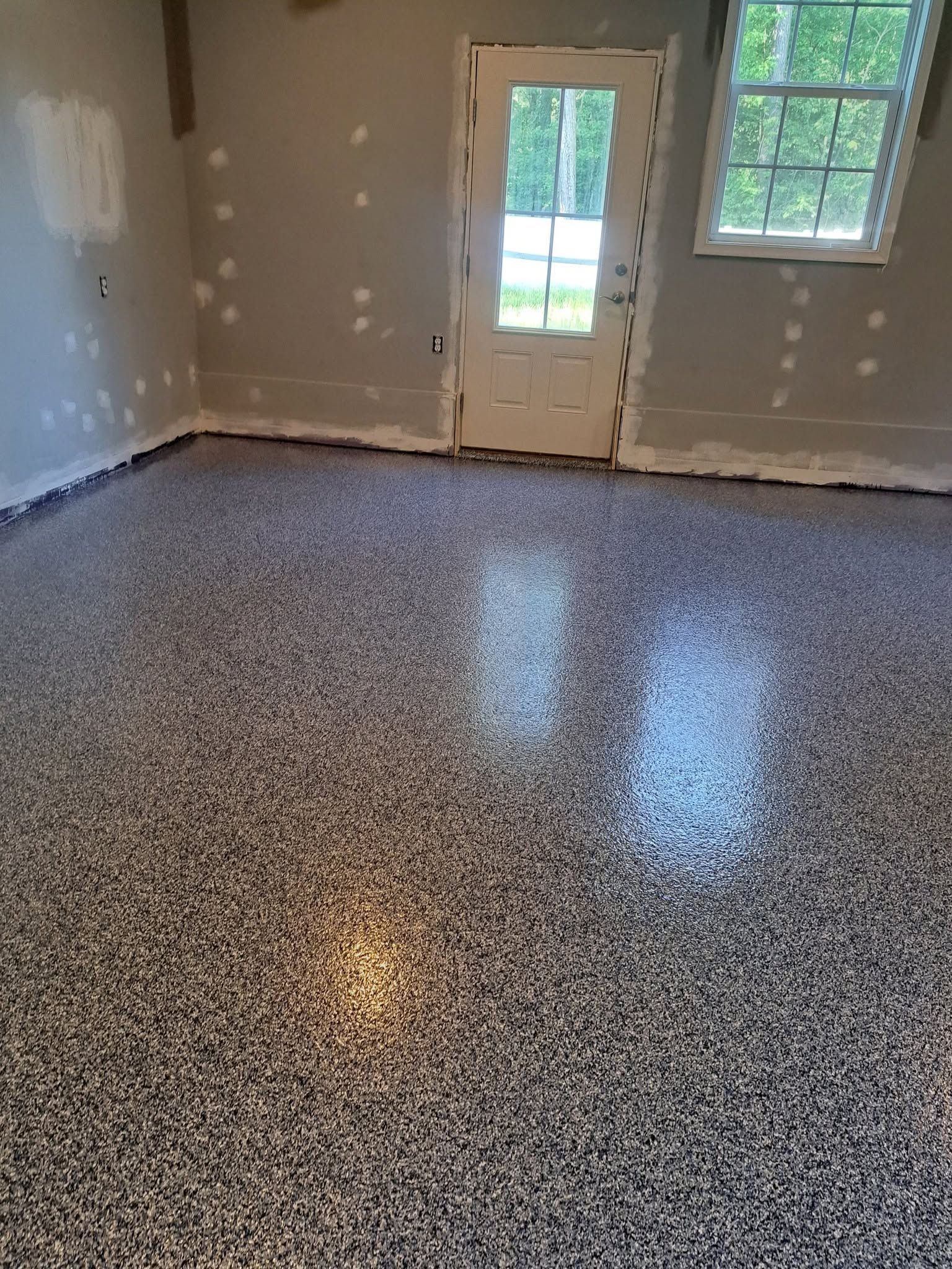 Empty room with speckled epoxy floor, gray walls, and a door leading outside