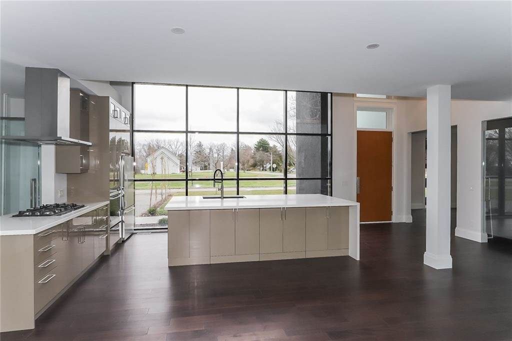 Modern open kitchen with white island, dark floor, and large windows overlooking a yard