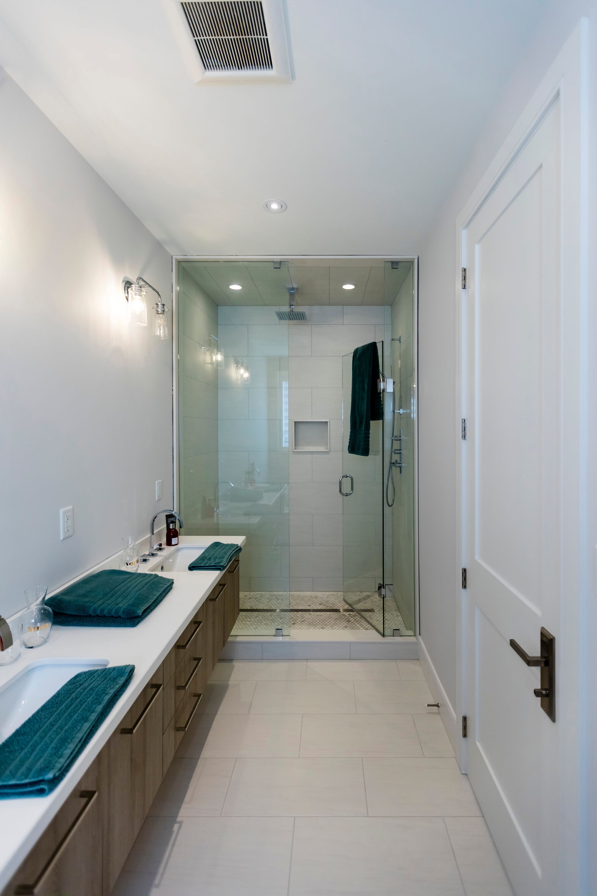 Bright bathroom with double sinks, large mirror, and glass shower at the back.