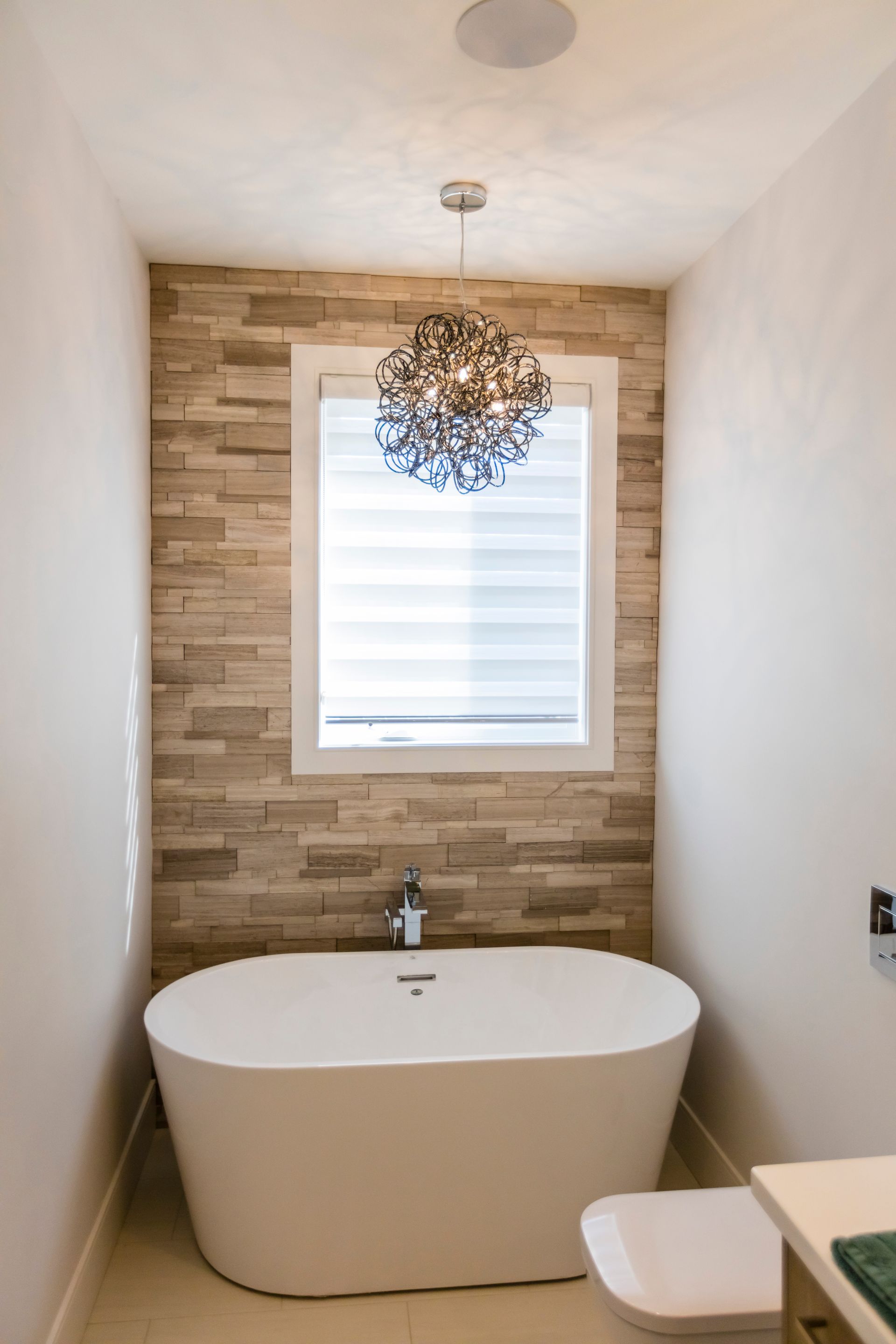 Modern bathroom with freestanding tub, window, and stone accent wall