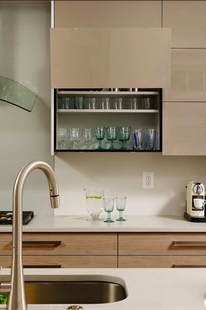 A kitchen with a sink , faucet , and a shelf with glasses on it.