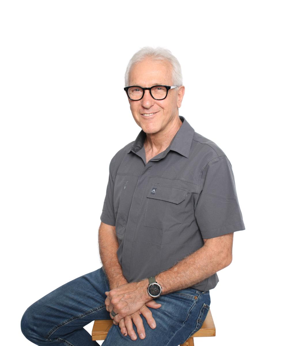 Smiling man in glasses and a gray shirt sitting on a stool against a white background
