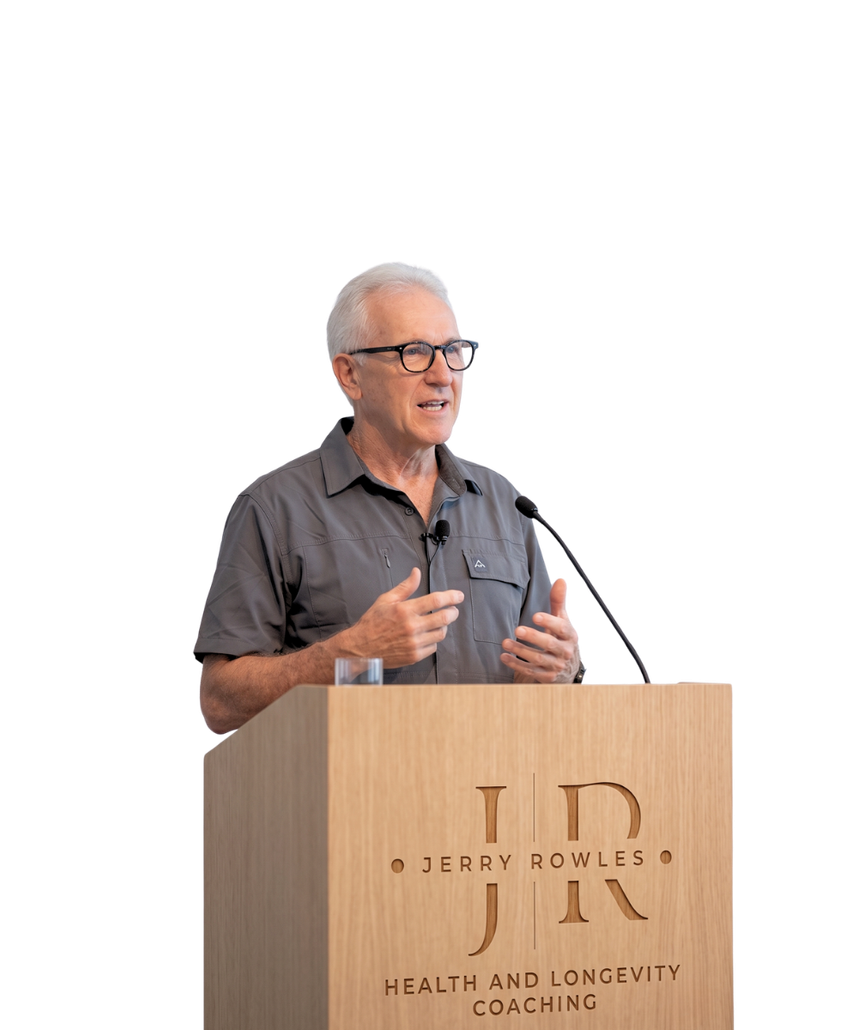 Man speaking at a podium with microphones, wearing glasses and a gray shirt, on a white stage background