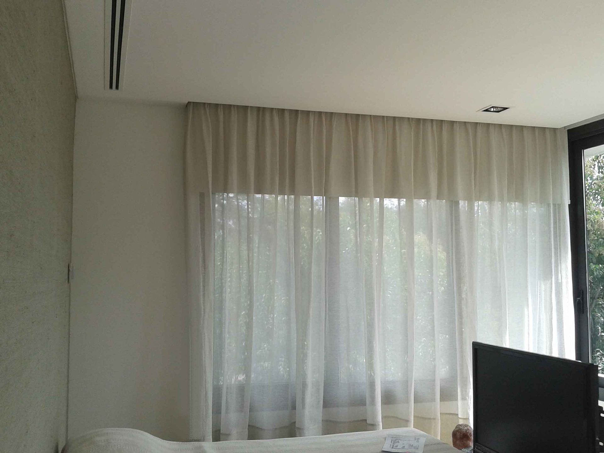 Un dormitorio con una cama, televisión y cortinas.