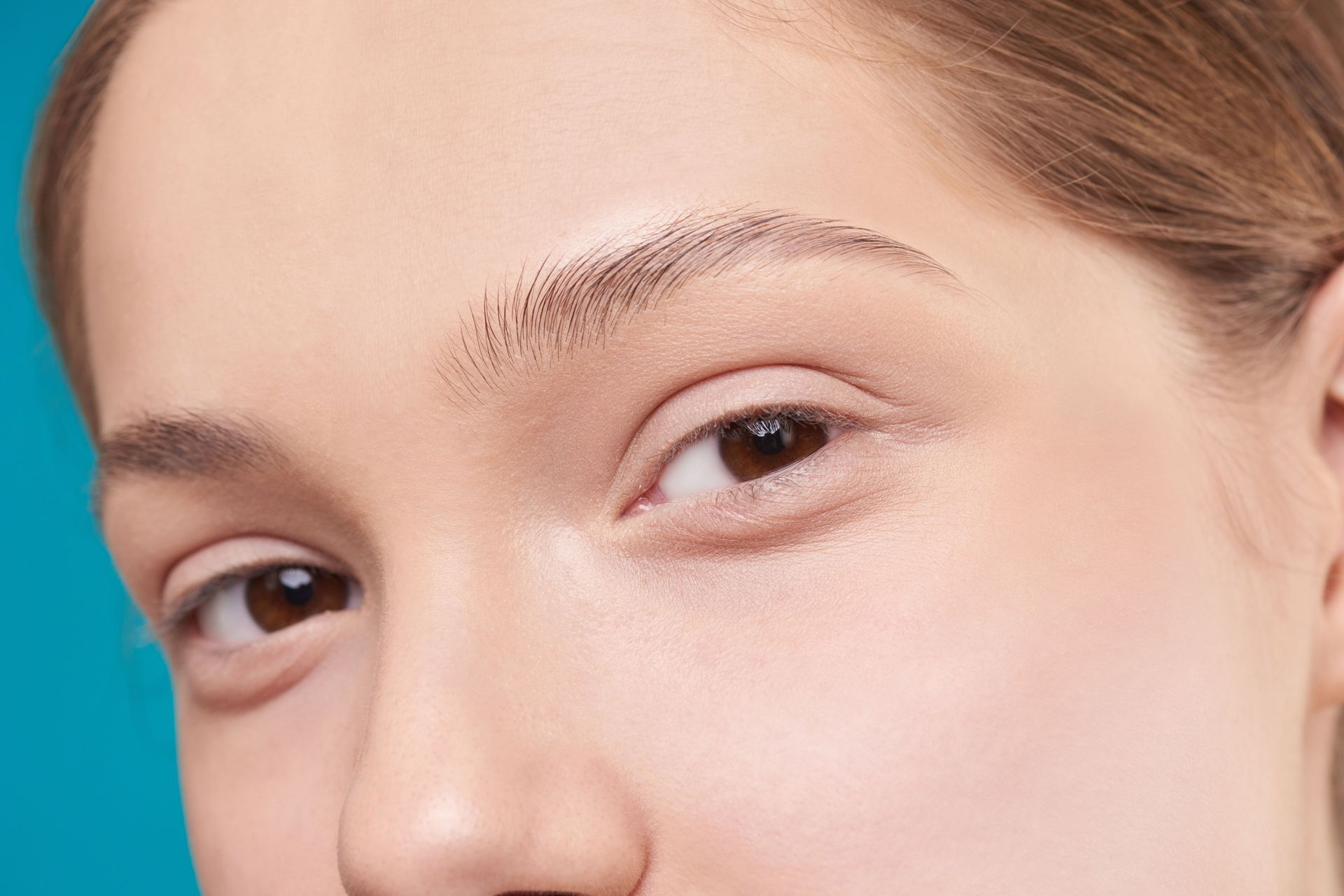 Close-up of a face showing one eye, eyebrow, and nose against a teal background