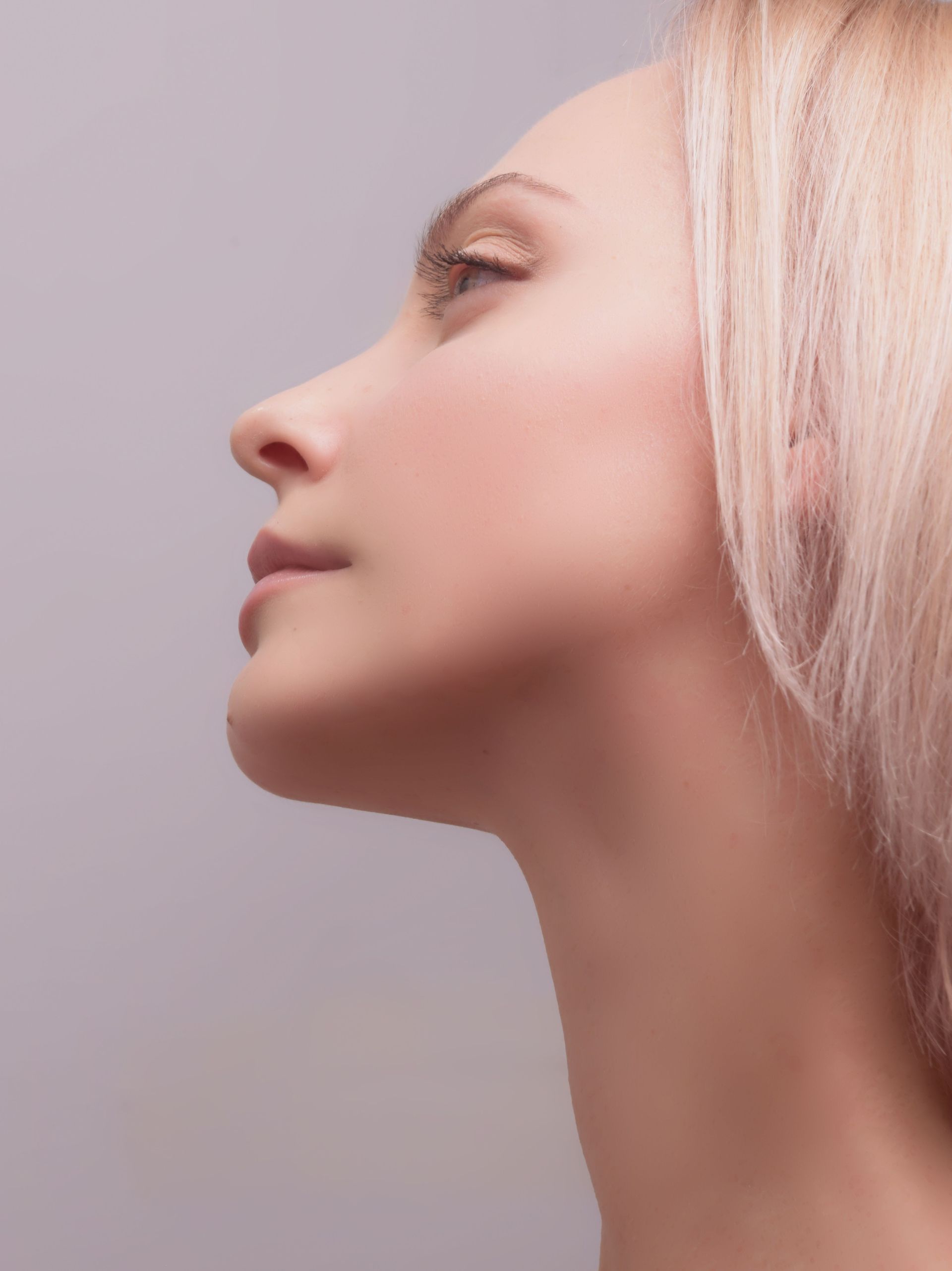 Side profile of a person with closed eyes against a soft gray background, wearing light blonde hair