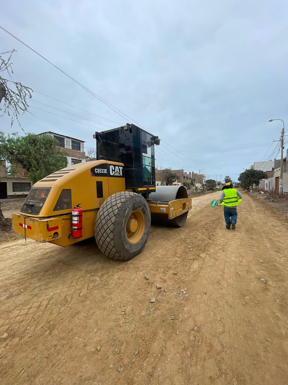 Apisonadora amarilla en un camino de tierra con un trabajador con chaleco reflectante cerca