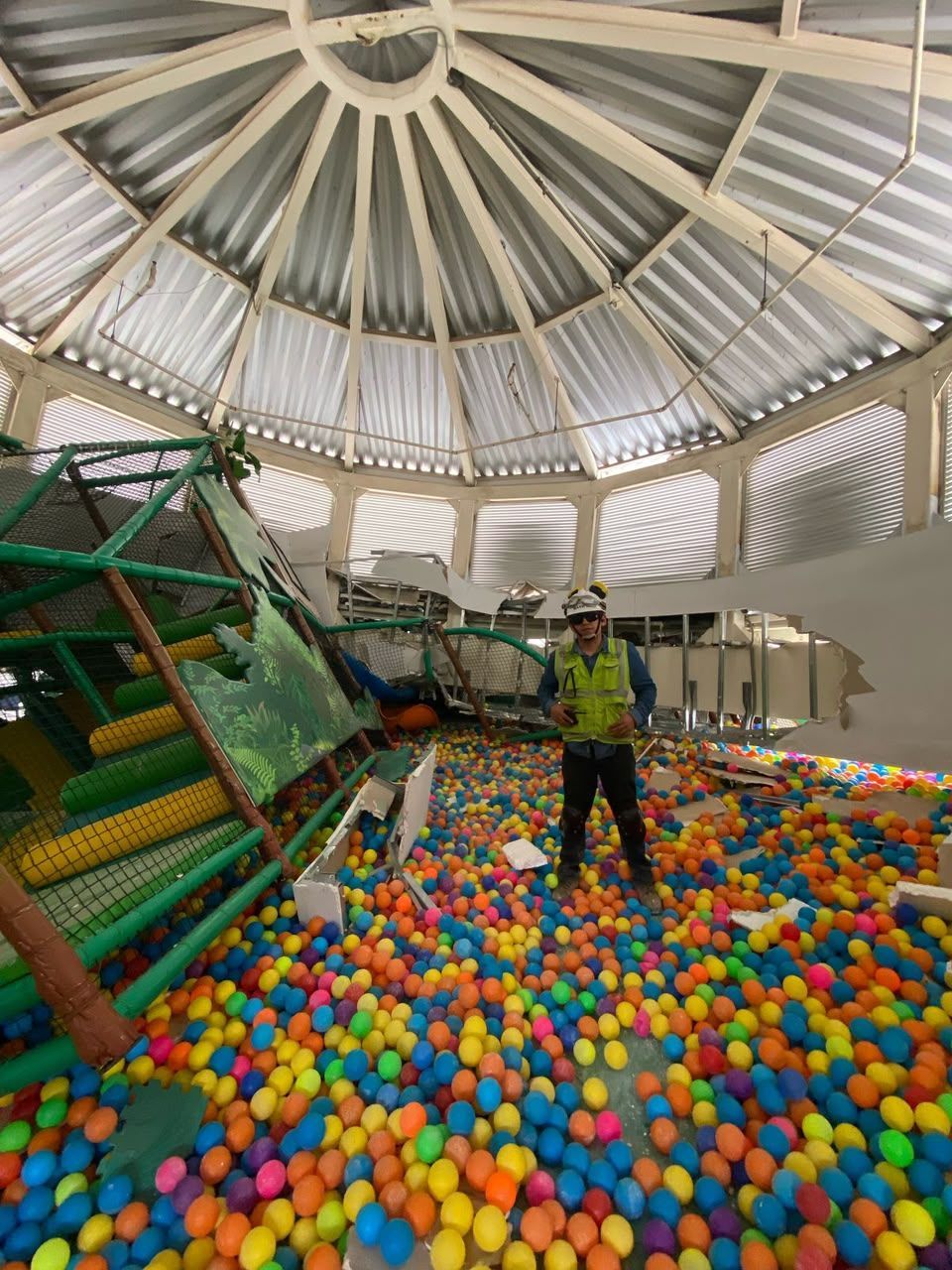 Piscina de bolas interior con un niño en un equipo de escalada bajo un gran techo abovedado.