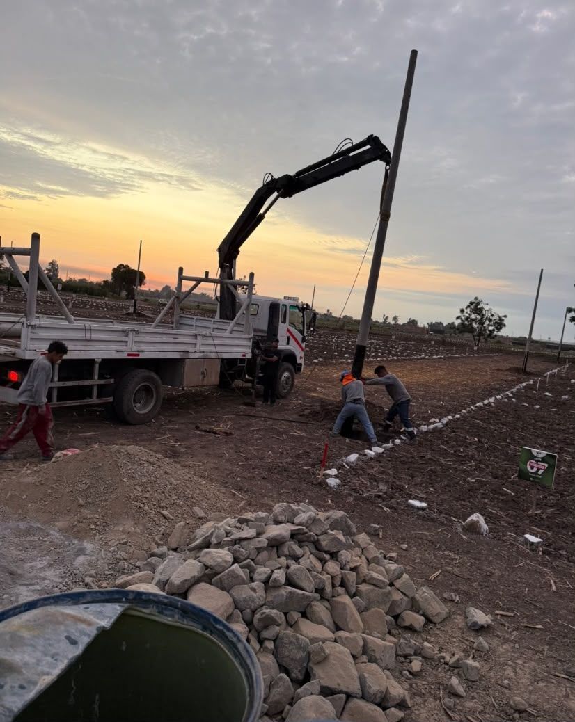 Trabajadores y una grúa montada sobre camión en una obra de construcción de tierra al atardecer.