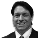 Man in suit smiles, looking at the camera.