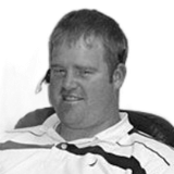Man in a wheelchair, smiling, wearing a polo shirt, and looking at the camera.