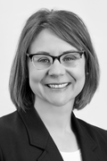 Woman with glasses smiles wearing a dark blazer.