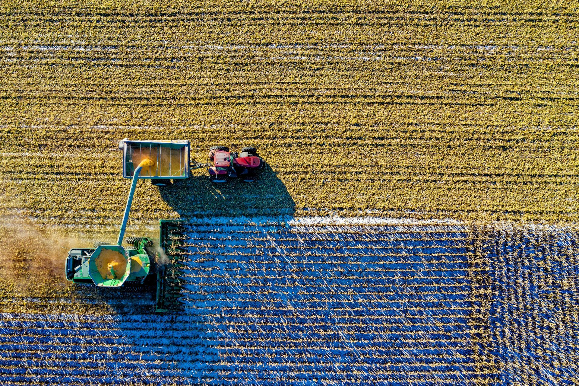 Aerial view: Tractor harvesting a crop in a field. Sections of the field are different colors, likely harvested or unharvested.