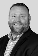 Man with a beard smiling, wearing a patterned shirt and blazer.