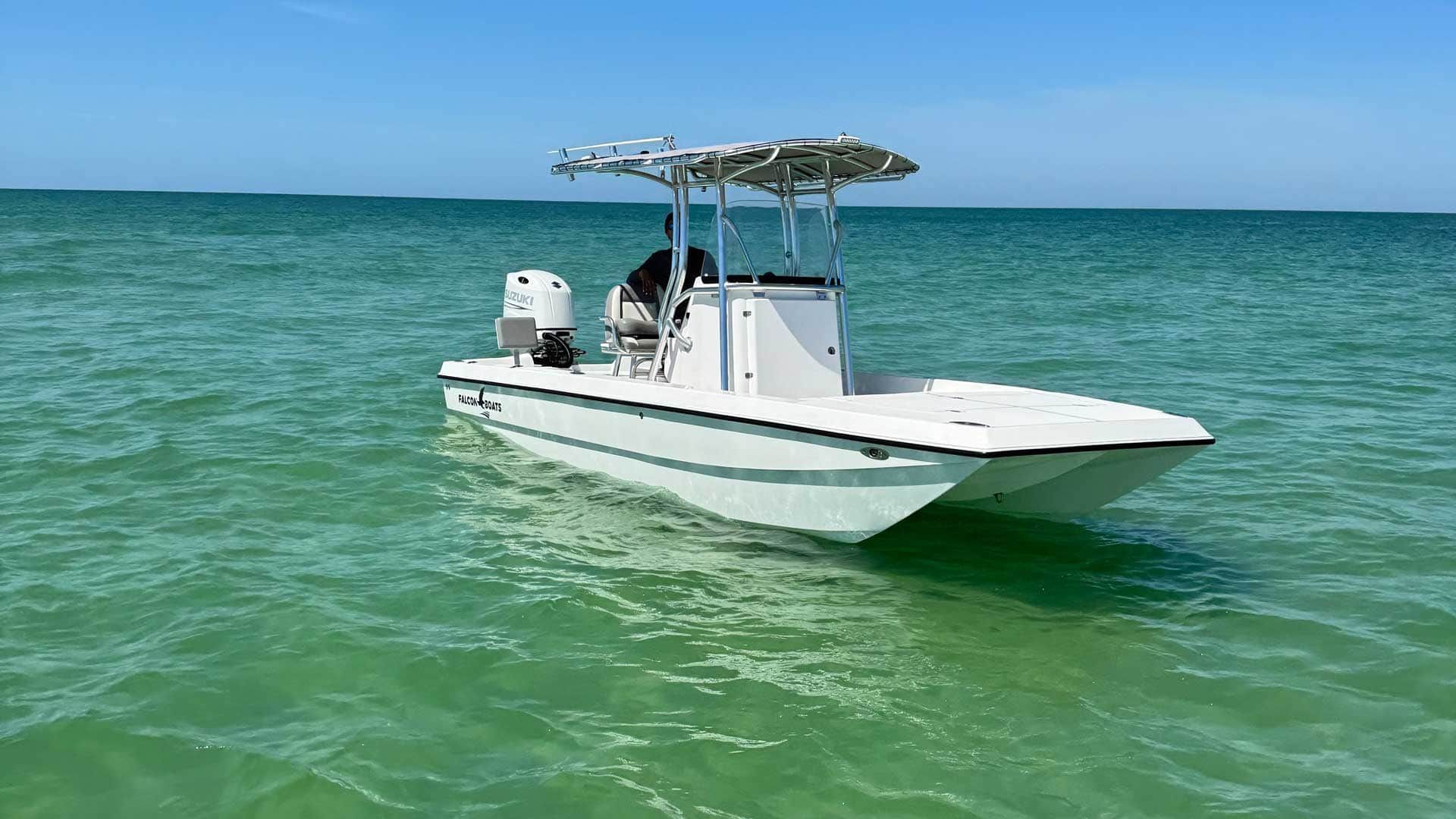 White boat on turquoise water under a blue sky. A person is in the captain's seat.