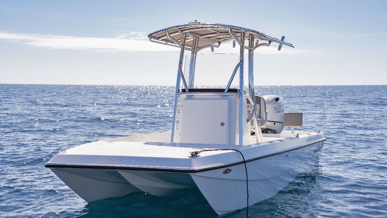 White catamaran boat floating on the ocean under a clear blue sky. It has a white metal frame structure.