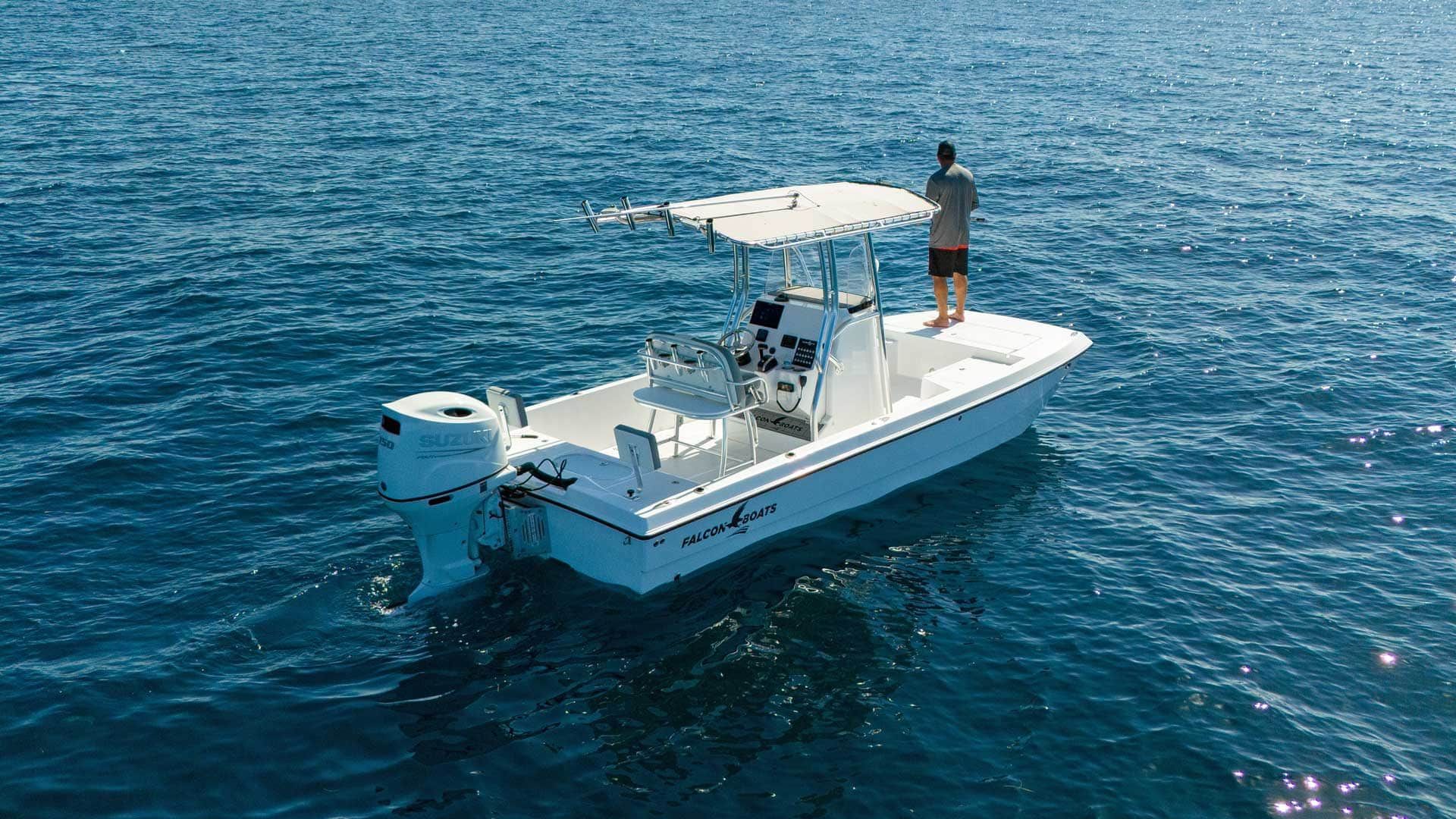 White fishing boat on blue water; a person stands on the boat's stern, fishing.