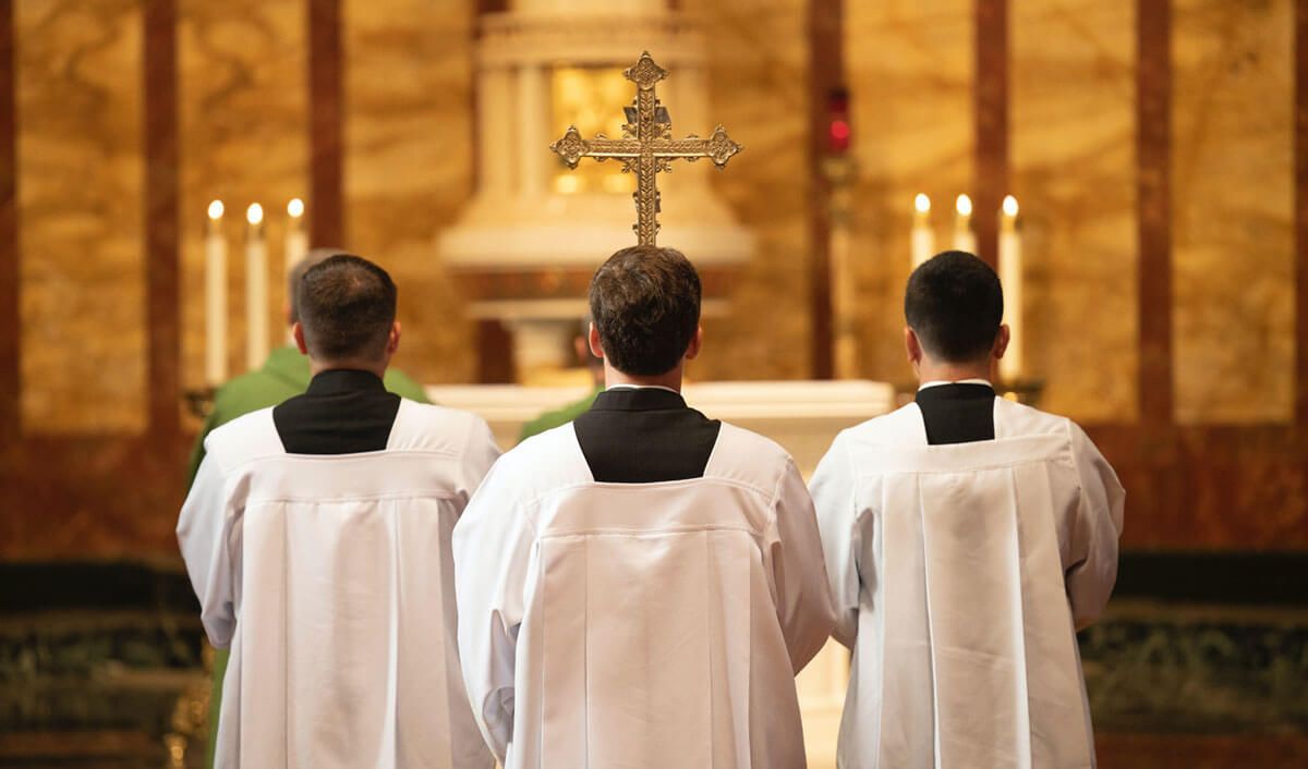 Three priests standing reverently before a casket