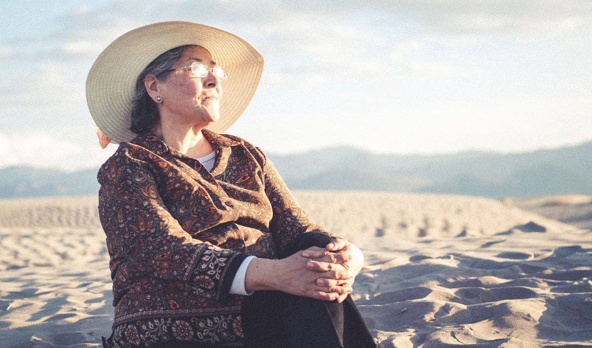 elderly woman sitting in sandy plains staring off into the horizon