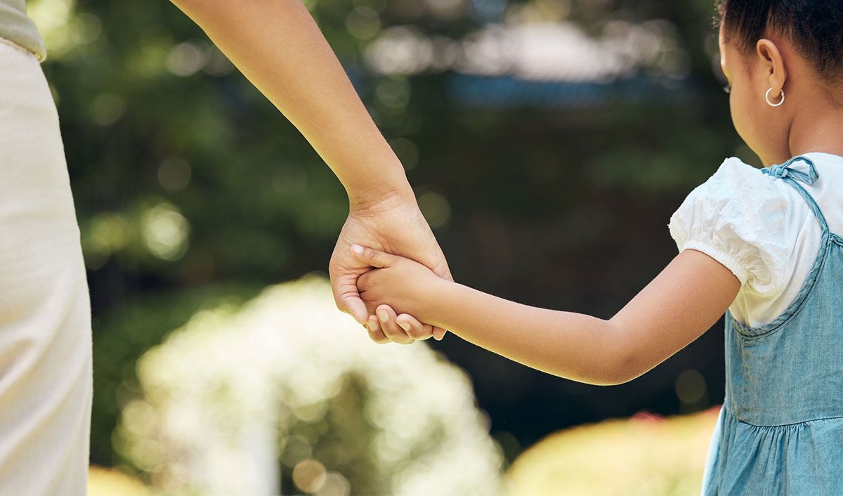 A little girl in a dress holds her mother’s hand as they walk.