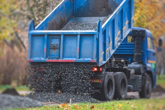 Blue dump truck unloading gravel onto a wet roadside