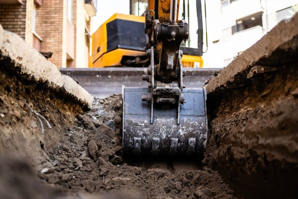 Excavator digging a trench with a large metal bucket on a construction site