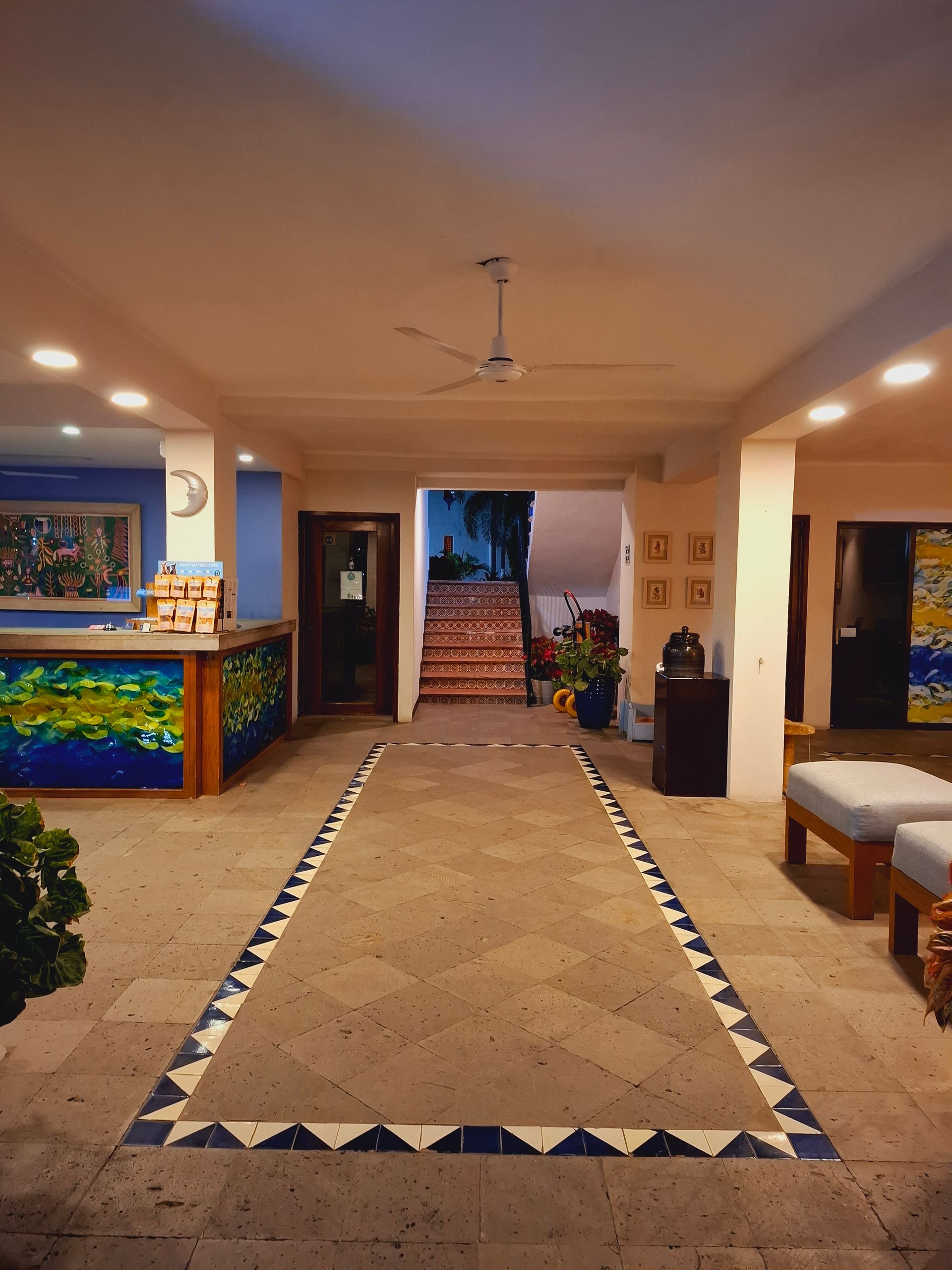 Open-air lobby with tiled walkway, reception desk, benches, and potted plants at dusk.