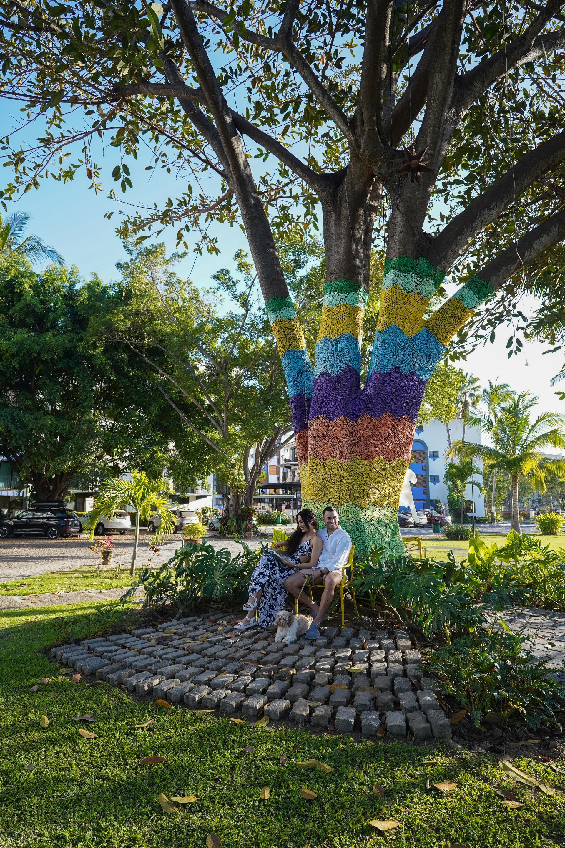 People sitting under a tree trunk painted with colorful stripes in a park setting.