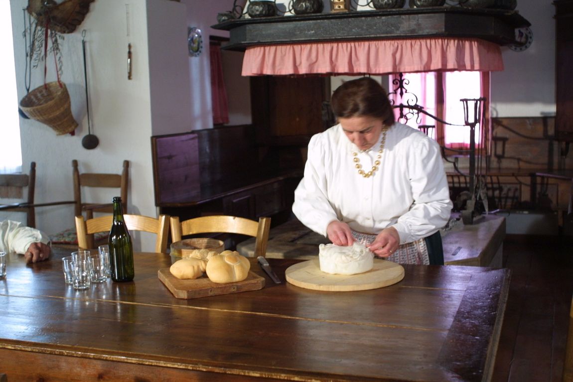 In una cucina rustica, una persona impasta il pane su un tavolo di legno, con pane e vino nelle vicinanze.