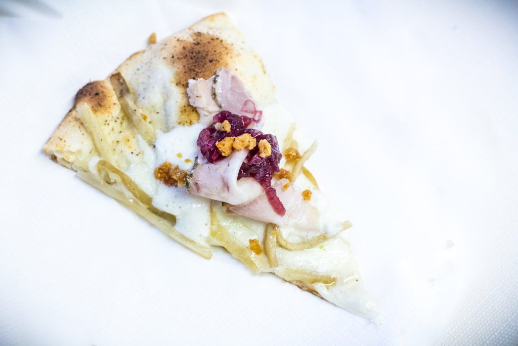 Fetta di pizza dolce con glassa bianca e guarnizioni viola su un piatto bianco.