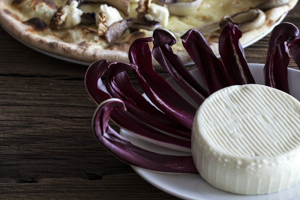 Foglie di indivia viola e una forma rotonda di formaggio bianco su un piatto, con uno sfondo di tavolo in legno scuro.