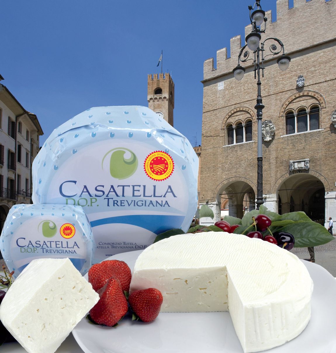 Forme di formaggio Casatella con fragole davanti a un edificio storico in pietra e al cielo azzurro.