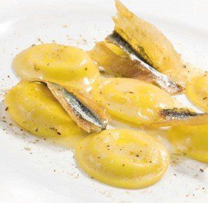 Conchiglie ripiene gialle con ripieno di pesciolini argentati, servite su un piatto bianco.