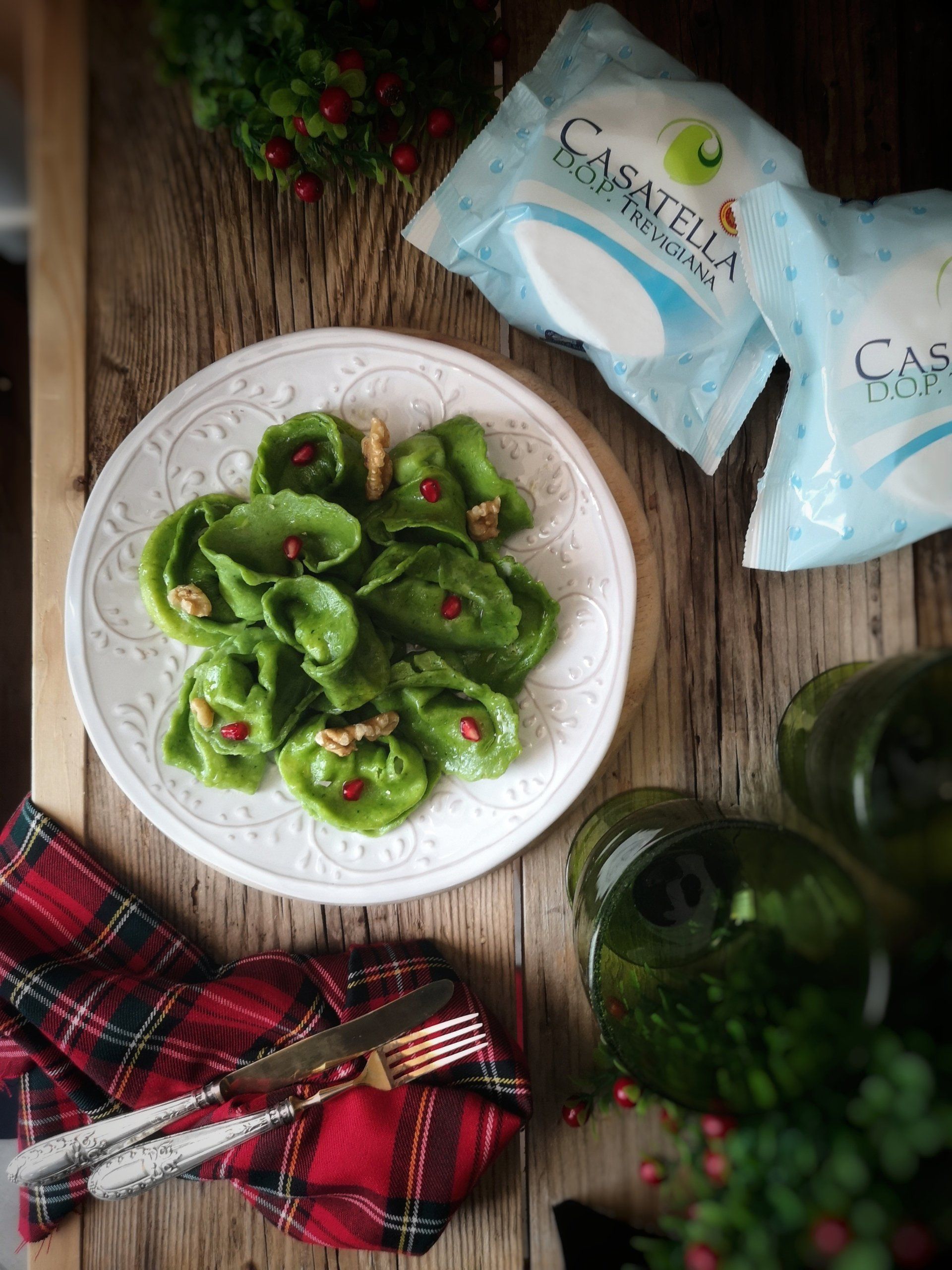 Tortellini verdi su un piatto bianco con pasta confezionata, un tovagliolo a quadri e verdure su un tavolo rustico.