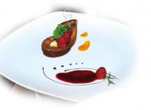 Elegante dessert impiattato con fragole, salsa all'arancia e un sorriso di cioccolato su un piatto bianco.