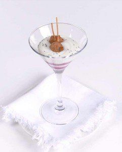 Bicchiere da Martini con un dessert cremoso guarnito con briciole di biscotti e bastoncini di cialda su un tovagliolo bianco.