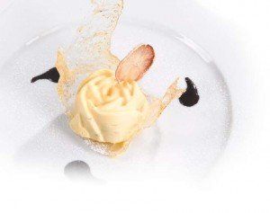 Pallina di gelato alla vaniglia con mandorla su un piatto bianco, decorata con salsa al caramello.