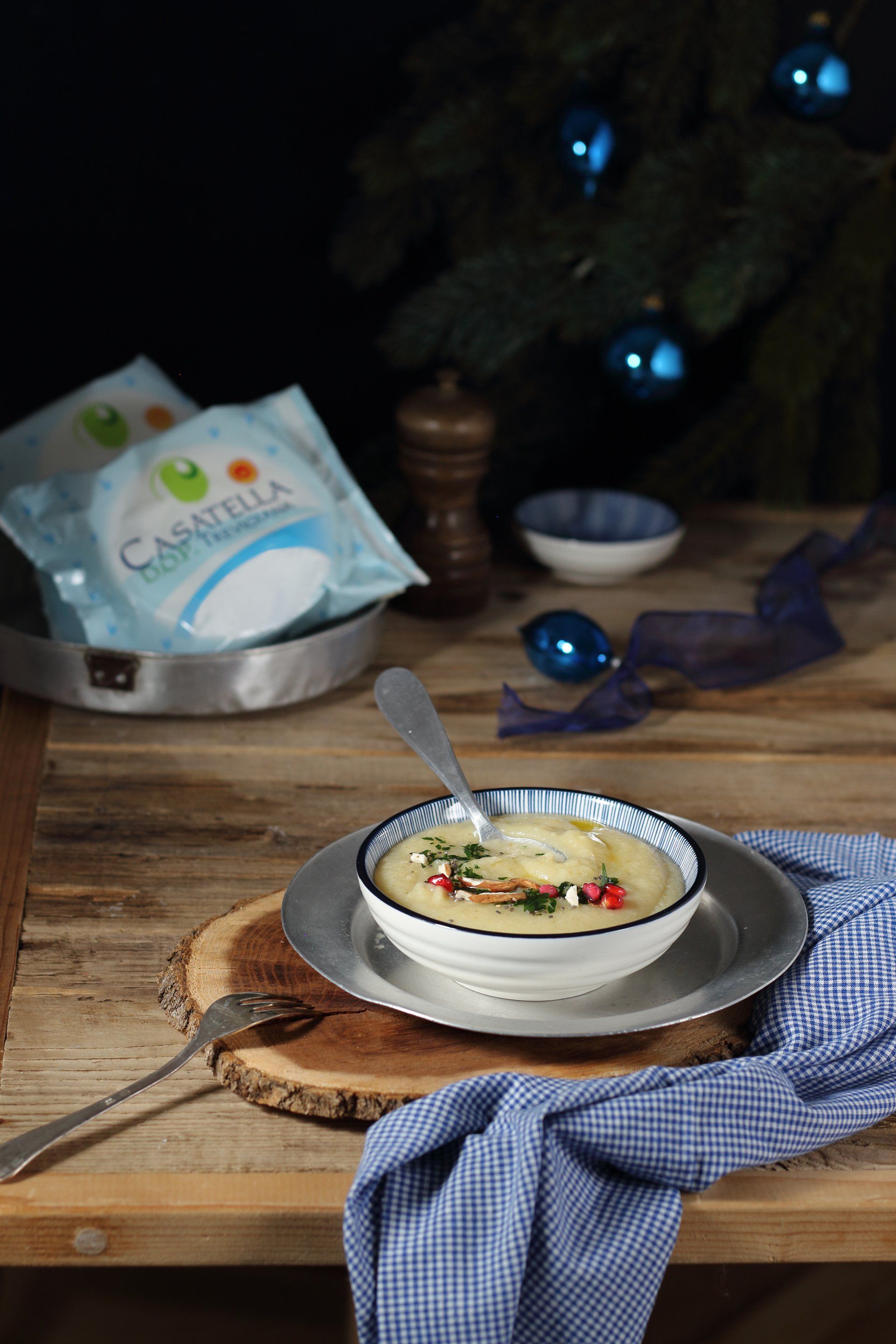 Dessert alla vaniglia in una ciotola su un tavolo di legno con un cucchiaio e una tovaglia blu, luci natalizie sullo sfondo.