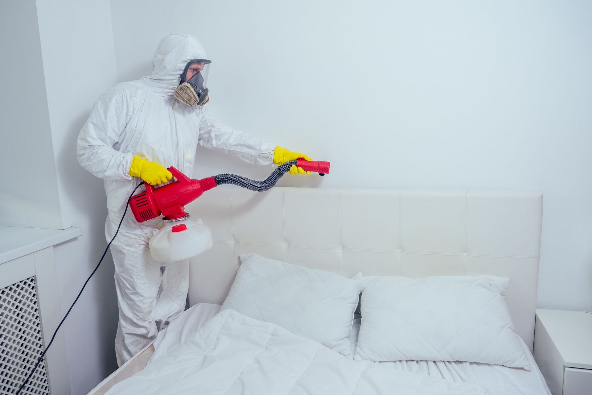 Pest control worker spraying pesticides in a bedroom.