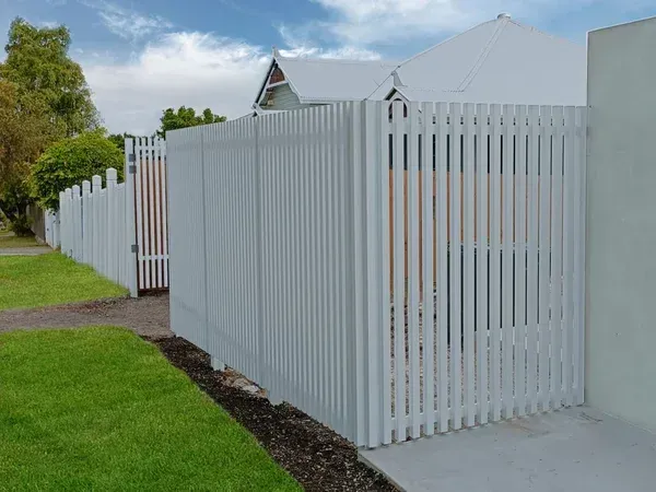 A white picket fence surrounds a driveway leading to a house.