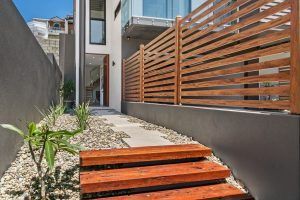 A wooden staircase leading up to a house with an aluminium wooden fence.