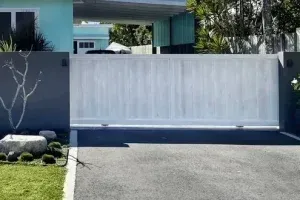 A white sliding gate is open to a driveway in front of a house.